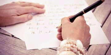 Person writing letters with black pen and white paper.