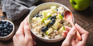5ff4d0e2d4e3d Bowl of oatmeal porridge with apple and blueberry. Female hands holding healthy breakfast oatmeal bowl