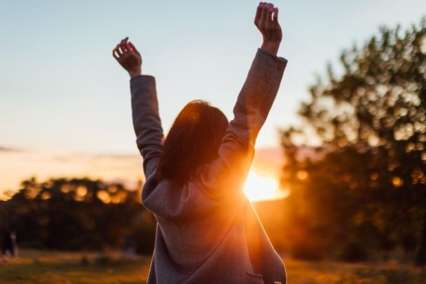 Rear View Of Young Woman Stretching Arms Against Sunset In The Sky. Rear view of young woman stretching arms against sunset in the sky.