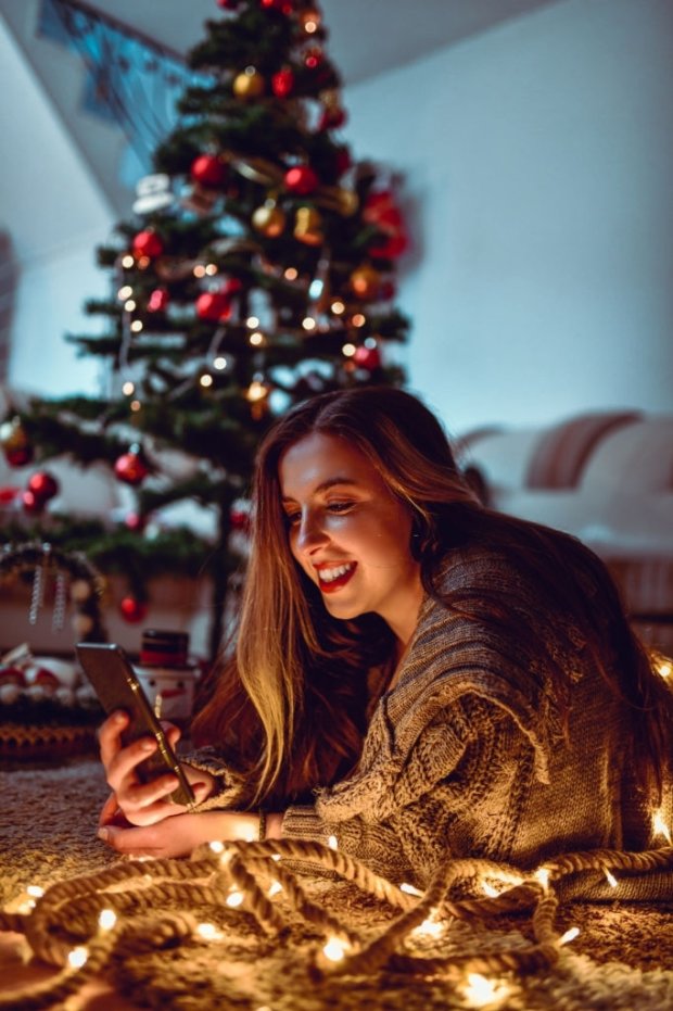 Female Relaxing With Smartphone And Lights On Christmas Eve