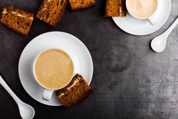 Two cups of fresh cappuccino with slice of carrot cake on gray background viewed from above