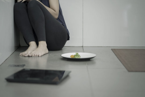 Portrait of lonely woman sitting with a plate of salad and weight scales in the bathroom. Weight loss concept