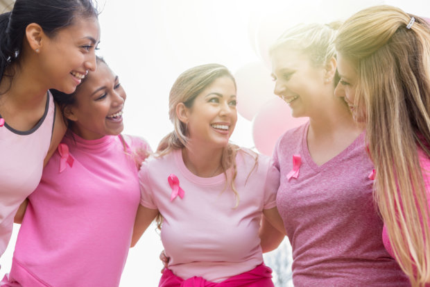 From the point of view of a woman in the huddle, a group of women stand arm in arm in a huddle and talk before a breast cancer awareness race.